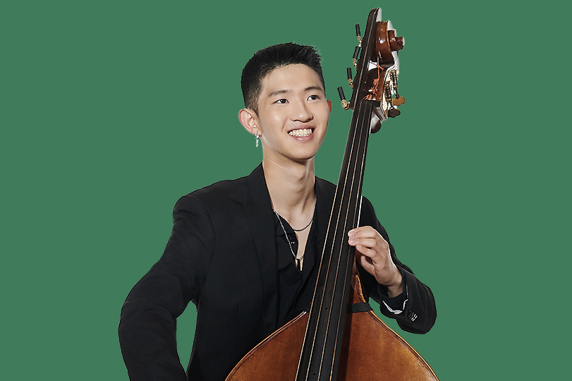 A student dressed in black playing the double bass with a dark green background